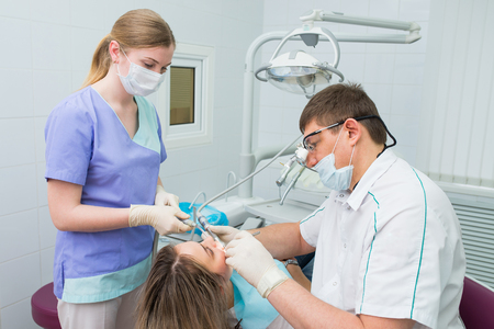 dentists and assistant treating teeth of woman patientの写真素材