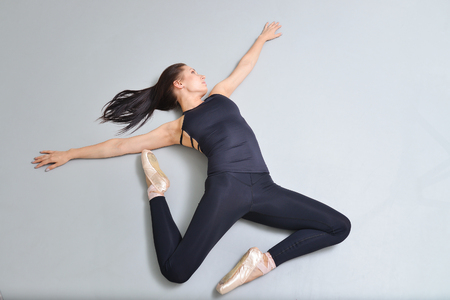 Young woman ballerina lying and stretching on the floor at ballet studio, view from above. Modelling fly or jump in air.の写真素材