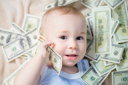 Cute baby boy playing with a lot of money like talking on telephone, american hundred dollars cashの写真素材