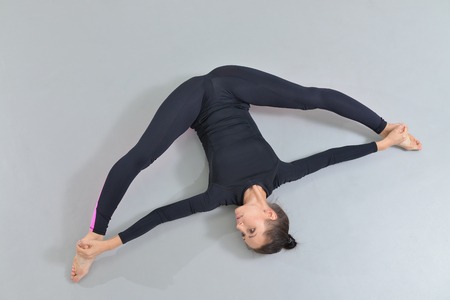 Beautiful woman in sportswear exercising at fitness studio, performing twine lying on the floor. High angle view.の写真素材