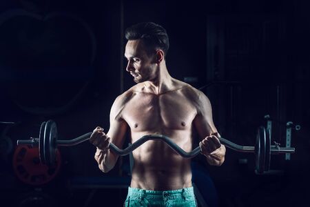 Strong Muscular man working out in gym doing exercises with barbell at bicepsの写真素材