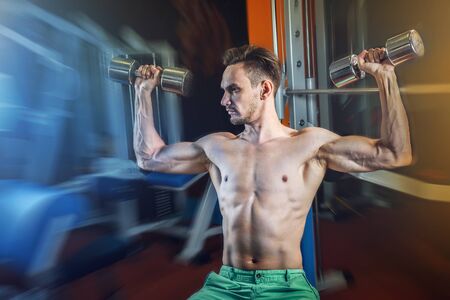 Handsome caucasian man working out at gym and doing shoulders exercises with dumbells.の写真素材
