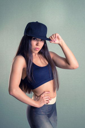 Fitness sporty cool girl wearing fashion sportswear. Brunette model with long dark hairs seriously looking at camera touching her cap visorの写真素材