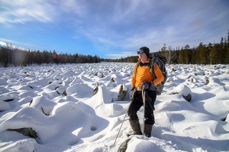 Hiker with backpack on the snow field of stones at he way to the rocky mountainsの写真素材