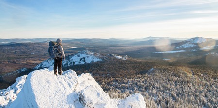 The mountaineer climbed the mountain top, man hiker standing at the peak of rock covered with ice and snow, view from back. Winter season.の写真素材