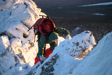 Woman hiker with backpack going thru rocks and snow on the mountain peak at cold winter day.の写真素材