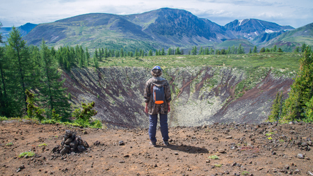 Young lady hiker standing back on top of old volcano crater enjoying view of beautiful summer landscape. Woman traveler with backpack on mountain peakの写真素材