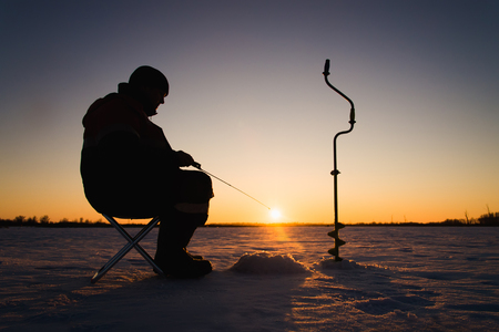 Silhouette of a fisherman on winter ice fishing at sunset.の写真素材