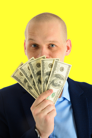 Happy handsome man in a suit holding fan of dollar banknotes, businessman and money. Isolated on yellow backgroundの写真素材