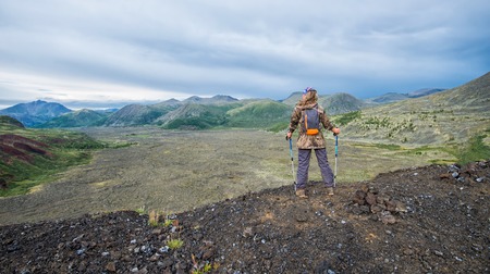 Lady hiker with backpack standing on top of the mountain, view from volcano peak to frozen lava valleyの写真素材
