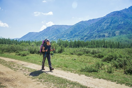 Young woman hiker with backpack and trekking poles on a sunny day on mountain trailの写真素材