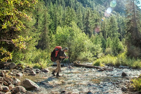 Hiker with backpack crossing mountain river. Hiking river crossing on the stones.の写真素材