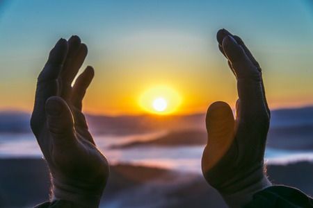 Hands of an old man reaching for the sun at sunrise, closeup. Concept of birth new lifeの写真素材