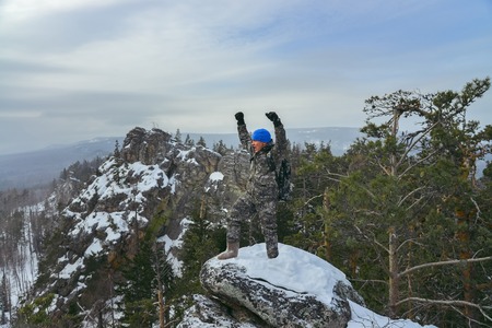 Happy man hiker standing at mountain top and celebrates success in winter dayの写真素材