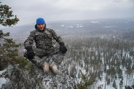 Man hiker sitting on rock in mountain at winter day and looking at cameraの写真素材