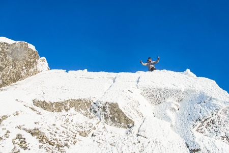 Happy The mountaineer climbed the mountain top covered with ice and snow, man hiker celebrating success at the peak of rock. Winter season.の写真素材