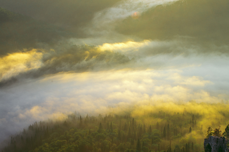 Mountain valley during golden sunrise. Fog and clouds over the forest highlighted by morning sun.の写真素材