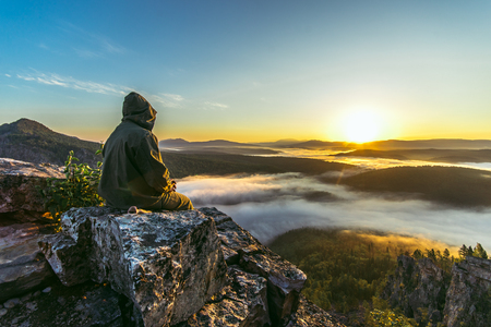 A tourist man sitting back on peak of mountains and meeting beautiful sunriseの写真素材