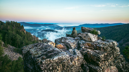Man traveller sitting on rock at mountain top and meeting sunrise, heavy mist in deep valley.の写真素材