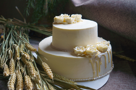 Wedding cream cake on rustic background. Beautiful Gourmet tart decorated with white roses and ears of wheat.の写真素材