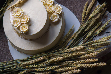 Wedding cream cake on rustic background. Beautiful Gourmet tart decorated with white roses and ears of wheat.の写真素材