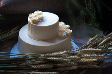 Wedding cream cake on rustic background. Beautiful Gourmet tart decorated with white roses and ears of wheat.の写真素材