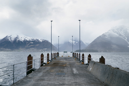 An empty ferry pier in a fjord with beautiful view to mountains covered with snow, scenic landscape in Norwayの写真素材