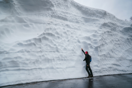 Young woman hiker with backpack amazed by large snow wall left after avalanche in mountains.の写真素材