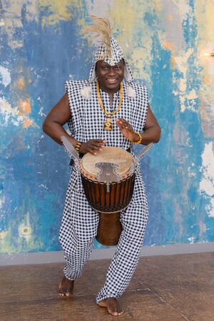 African artist in traditional clothes playing djembe drumの写真素材