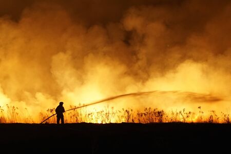 Silhouette of fireman fighting bushfire at night, man against the fire.の写真素材