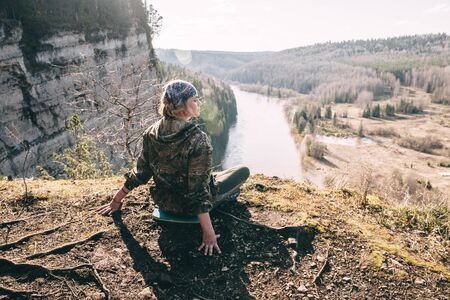 Beautiful young woman sitting at mountain top and looking at scenic landscape.の写真素材