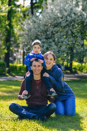 Happy family together in outdoor park at spring sunny day. Mom, dad and son in the garden. Group of people on green grass.の写真素材
