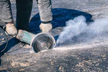 Circular saw cutting reinforced concrete slab during roof repair. Worker hands with with electric angle grinder closeupの写真素材
