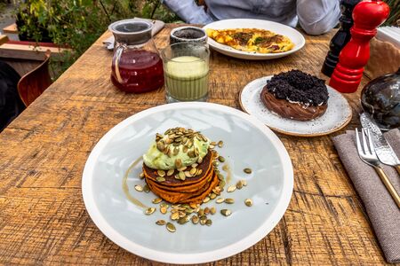 Breakfast in the cafe with sweet potato pancakes, matcha latte, curd ring, cranberry tea and omelette. wooden table.の写真素材