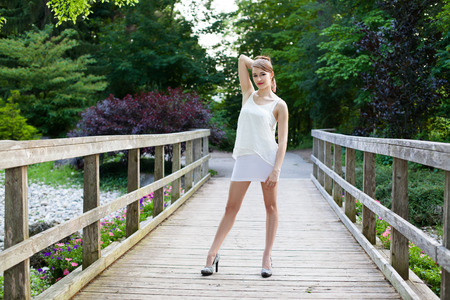 Beautiful girl is in on a wooden bridge. Casual and thoughtful in a park during summer.の写真素材