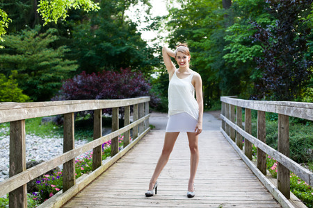 Beautiful girl is in on a wooden bridge. Casual and thoughtful in a park during summer.の写真素材