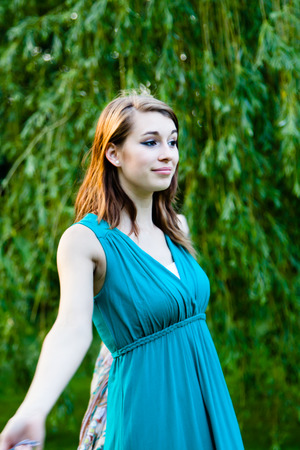 Beautiful girl is in front of a willow tree. Carefree, happy and joyful in a park during summer.の写真素材