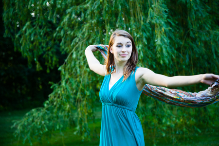 Beautiful girl is slowly spinning around in front of a willow tree. Carefree, happy and joyful in a park during summer.の写真素材