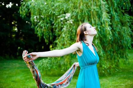 Beautiful girl is slowly spinning around in front of a willow tree. Carefree, happy and joyful in a park during summer.の写真素材
