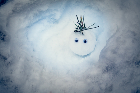 The snowball-sized snowman looks with surprise as it sits in the snow.の写真素材