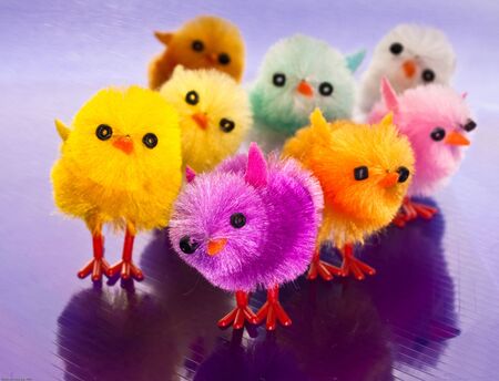 Orange, purple, pink, blue, yellow toy chicks on a striped surface