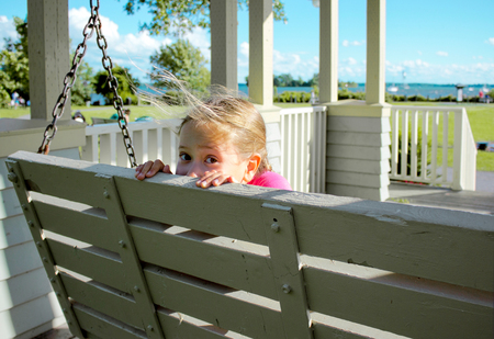 Playful girl hiding on swing bench in the parkの写真素材