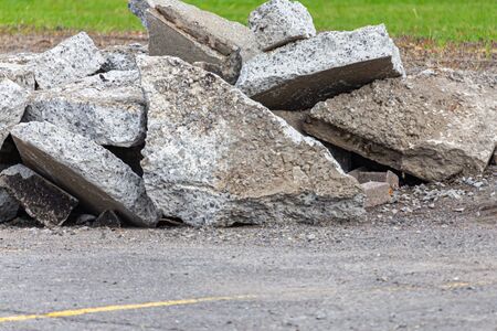 Fragments of broken asphalt and concrete are piled on the ground in a parking lot. The stone shards were dug up and torn out of the ground by an excavator during construction to renovate the pavement.の写真素材
