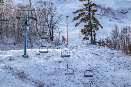 A chairlift is seen on the side of a ski hill, its seats hanging empty and motionless as the hill is prepared for skiers and snowboarders ready to hit the slopes.の写真素材