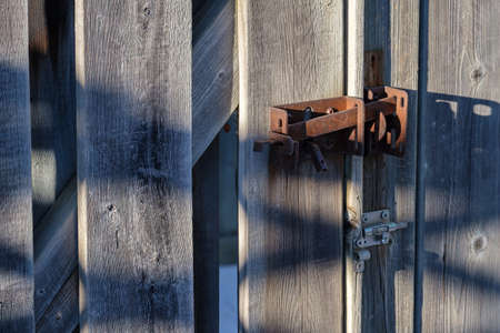 A rusted metal latch holds the gate of a wooden fence shut.の写真素材