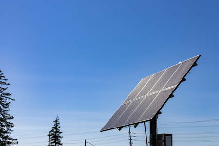 A free standing array of solar panels is pointed up at a clear blue sky. Power lines can be seen behind it in the background.の写真素材