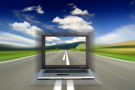 Road among green fields with motion blur effect and laptop, blue sky in the backgroundの写真素材