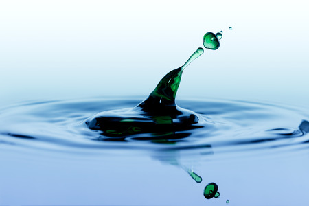 Splash. Green drop falling on smooth surface of water.の写真素材