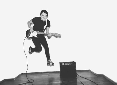 Awesome crazy fashion young musician rock guitar player jumps with passion in studio. Stylish rocky emotional man. Black and white toned.の写真素材