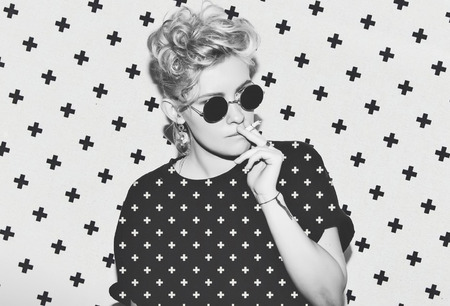 Contrast pattern stylish fashion sexy blonde bad girl in a black t-shirt and rock sunglasses. Dangerous rocky emotional woman. white toned. background, not isolatedの写真素材